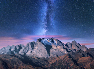 Milky Way over mountains in fog at night in summer. Landscape with alpine mountain valley, purple low clouds, colorful starry sky with milky way. Passo Giau, Dolomites, Italy. Space. Beautiful nature