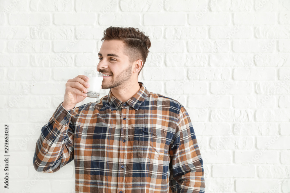 Handsome man drinking tasty milk on white brick background