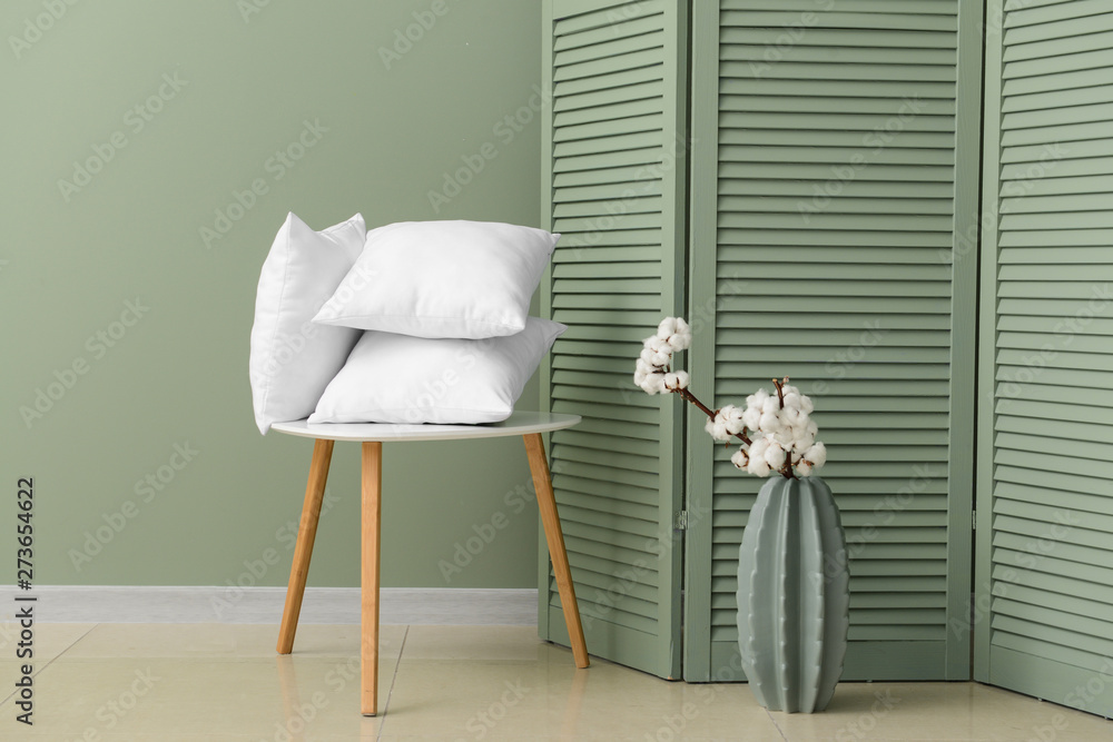 Table with soft pillows and vase with cotton flowers in room