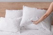 © Pixel-Shot - Woman fluffing soft pillows on bed
