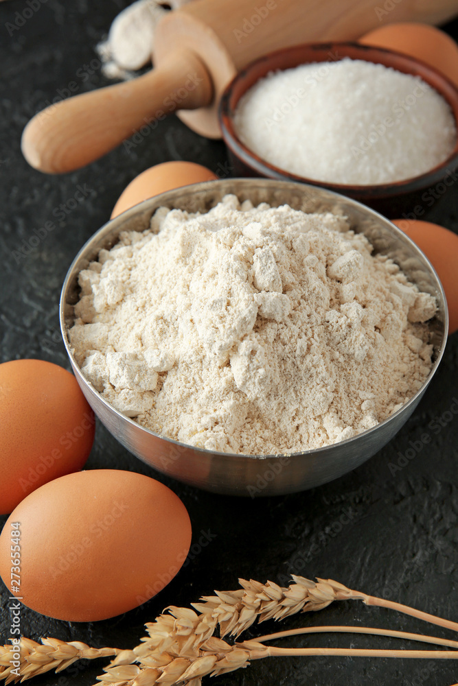 Bowl with flour and products on dark background