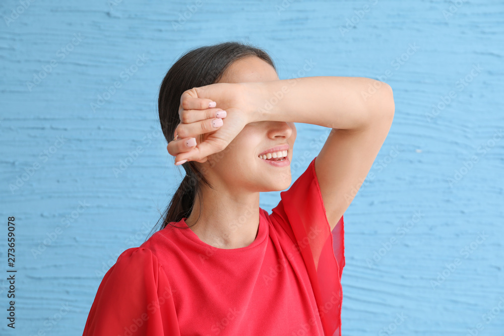 Young woman covering her eyes on color background