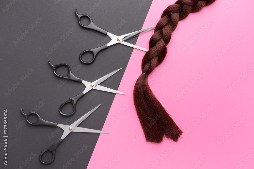 Braided hair strand and scissors on color background