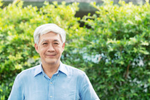 Headshot Of Happy Old Mature Asian With White Grey Hair Man Wearing Blue Shirt Smiling Positive And Looking At Camera In Garden Outside The House. Senior Asian Male Portrait With Retirement Concept.