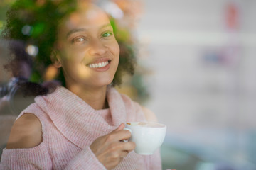 Wall Mural - Gorgeous mixed race woman in pink turtleneck sweater standing in coffee shop, drinking espresso and looking trough window.