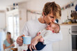 © Halfpoint - Young father holding a newborn baby in kitchen at home, kissing.