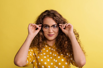 Wall Mural - Portrait of a young woman with glasses in a studio on a yellow background.