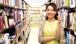 © Syda Productions - education, reading and knowledge concept - happy asian young woman pointing finger up over book shelves in library background