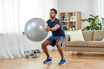 fitness, sport and healthy lifestyle concept - indian man exercising and doing squats with ball at home