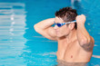 © herraez - Handsome muscular man standing inside the pool putting on his swimming googles .