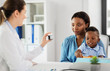 medicine, healthcare and pediatry concept - caucasian doctor giving medication to african american mother with baby son at clinic