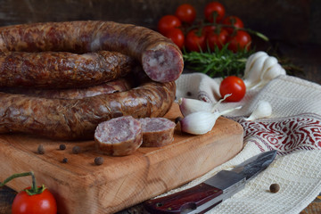 Traditional smoked sausage ring in a rustic style. Appetizing sausages made of pork and lamb with fresh herbs, spices on the wooden board. Free space for text.