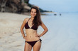 © romannoru - Happy girl with perfect body in black swimwear posing on white sand beach