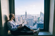 © BullRun - Happy smiling female tourist enjoying scenic views from hotel window of famous New York landmark during her vacation holidays. Attractive hipster girl sitting with digital tablet in coworking office