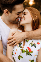 Wall Mural - Close up portrait of a handsome couple embracing and smiling before kissing outside against sunset.