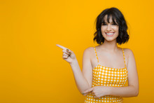 Portrait Of A Amazing Girl With Dark Short Hair Pointing Awaint With Finger Laughing Dressed In Yellow Against A Yellow Background.