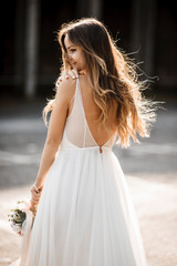 Back view portrait of a beautiful young bride with long hair holding a bucket and looking over the shoulder smiling against sunrise