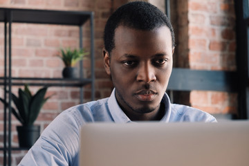 Wall Mural - Close-up portrait of serious and concentrated african man working with laptop at modern loft office