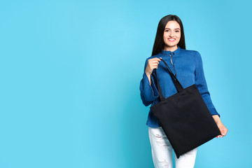 Beautiful young woman with stylish blank eco bag against color background, space for text