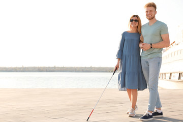 Young man helping blind person with long cane in city. Space for text