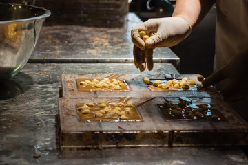 Producing milk chocolate bars. Hand adding hazelnuts (nuts) into the chocolate bar. Action. Low light. Small business - candy shop.