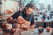 Diligent man is putting colourful clay to his new handmade pot.