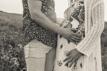 Wall Mural - Pregnant young girl in the last month of pregnancy with her husband in a poppy field and supports her abdomen hands at sunset