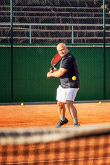 Wall Mural - A middle-aged bald man emotionally plays tennis on the court. Outdoor. Vertical.