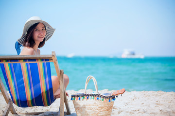 Summer time woman vacation on the beach. Cheerful woman wear summer dress and straw hats sitting on the beach look at sea. Time to relax in summer lifestyle outdoor shot on tropical island beach.