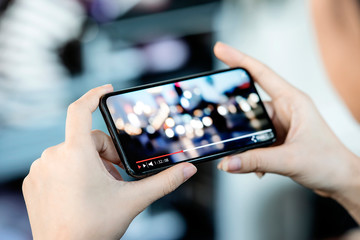 cropped image of female hand holding smartphone and watching video while standing outdoor.