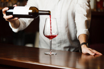 Wall Mural - Male sommelier pouring red wine into long-stemmed wineglasses.