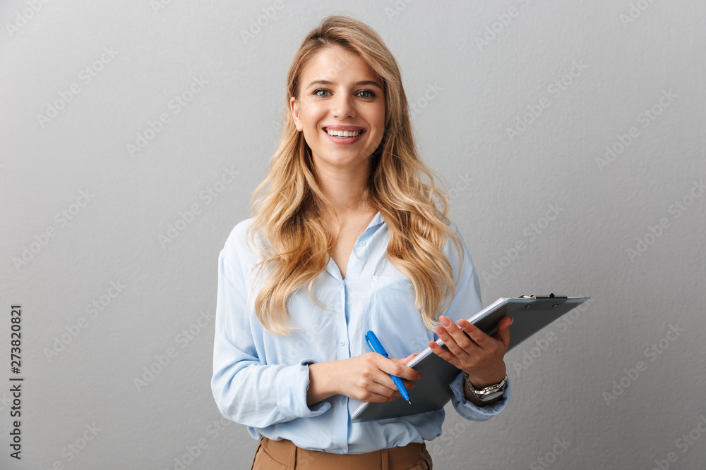 Photo of gorgeous blond secretary woman with long curly hair writing down notes in clipboard while working in office - obrazy, fototapety, plakaty 