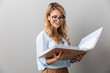 Photo of pretty blond secretary woman wearing eyeglasses smiling and holding file folder while working in office