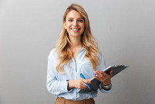 Photo Of Gorgeous Blond Secretary Woman With Long Curly Hair Writing Down Notes In Clipboard While Working In Office