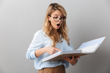 Poster - Photo of smart blond secretary woman wearing eyeglasses smiling and holding file folder while working in office