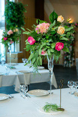 Beautiful table setting with crockery and flower arrangement in a vase on a high stem for a party, wedding reception or other festive event. Glassware and cutlery for catered event dinner