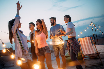 Happy friends with drinks toasting at rooftop party at night