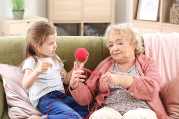 Cute little girl with grandmother knitting at home