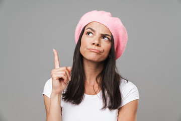 Wall Mural - Photo closeup of serious pretty woman in basic t-shirt and beret thinking while pointing finger upward at copyspace