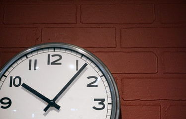 Classic clock with a white dial and black arrows on the background of a red brick wall.