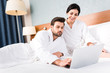 © LIGHTFIELD STUDIOS - bearded man using laptop near happy woman in hotel room