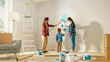 © Gorodenkoff - Beautiful Young Family are Showing How to Paint Walls to Their Adorable Small Daughter. They Paint with Rollers that are Covered in Light Blue Paint. Room Renovations at Home.