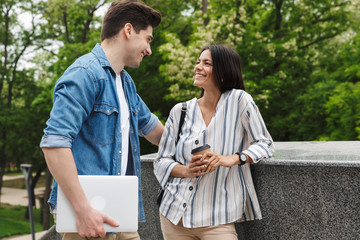 Canvas Print - Image of attractive couple with paper cup and laptop talking while standing on stairs outdoors