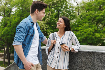 Sticker - Image of caucasian couple with paper cup smiling and talking while standing on stairs outdoors