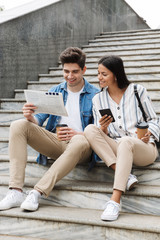 Poster - Happy young amazing loving couple business people colleagues outdoors outside on steps reading newspaper drinking coffee.