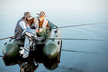 Grandfather with adult son fishing on the inflatable boat on the lake early in the morning