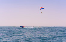 Ocean View Of A Man Parasailing In The Sea Towed By A Speedboat In American Colors - Watersports Summer Activity Of A Boat Towing A Parasail Above Water At Twilight With USA Stars & Stripes - Image