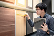 © zephyr_p - Asian man using digital tablet and tape measure for measuring on cabinet panel, choosing materials for built-in furniture design. Shopping furniture and house decoration. Home improvement concept