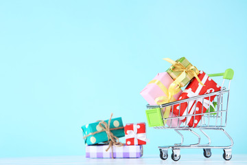 Wall Mural - Small shopping cart with gift boxes on blue background