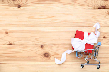 Poster - Small shopping cart with gift box on brown wooden table